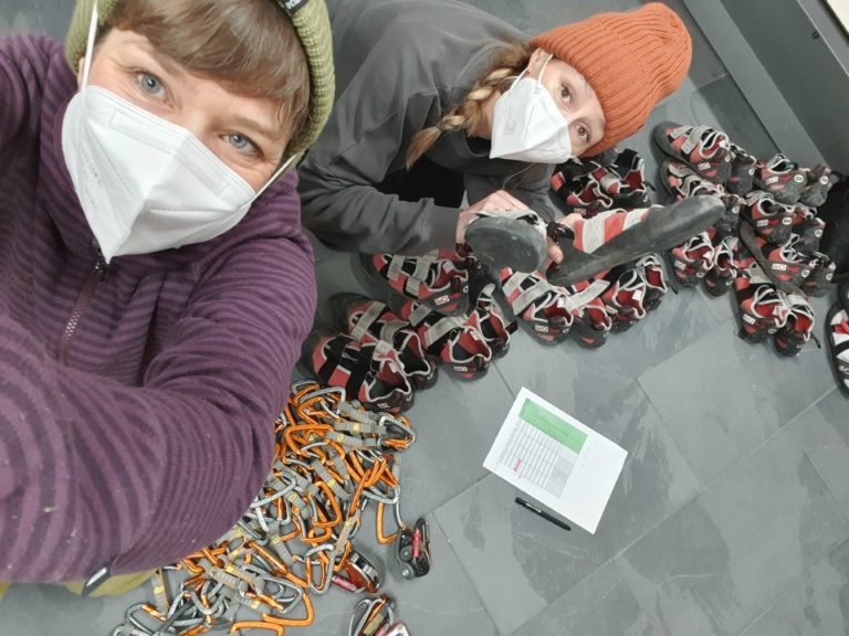 Das Bild zeigt Bekka und Nadja mit einer Checkliste vor einem Haufen Klettermaterial.