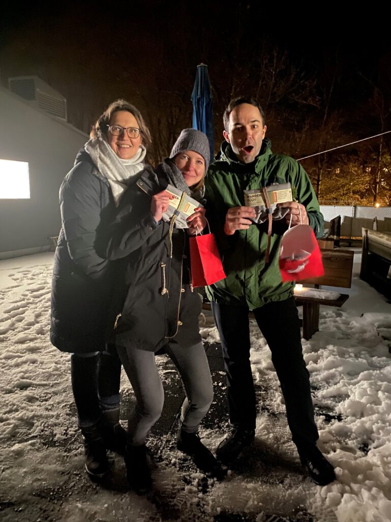 Friederike, Stephanie und Stefan im Schnee, am Abend, mit roten Tüten in der Hand.