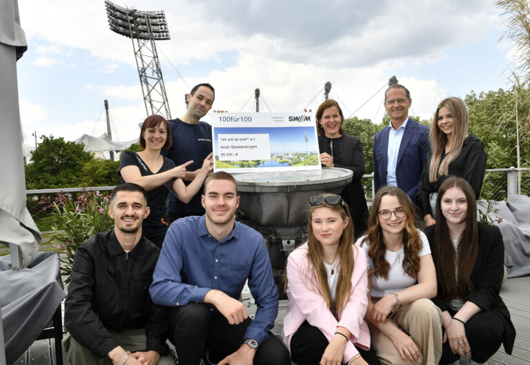 Eine Gruppe von 9 Menchen. Im Hintergrund das Olympiastadion in München. Zwei Personen halten einen großen Spendenscheck zwischen sich